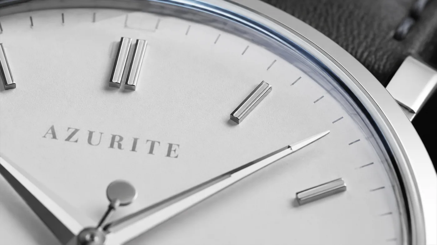 Macro of the Alba dial between twelve and three: polished indices on white lacquer and the AZURITE wordmark